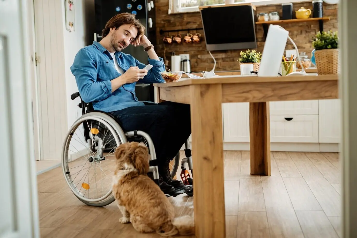 Low-angle shot of a smiling entrepreneur in a wheelchair texting on a mobile phone during a lunch break at home