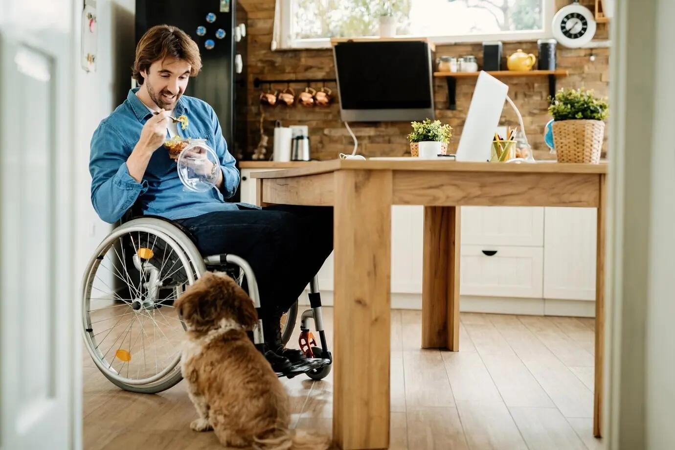 Smiling disabled freelance worker enjoying his lunch break with his dog while working from home