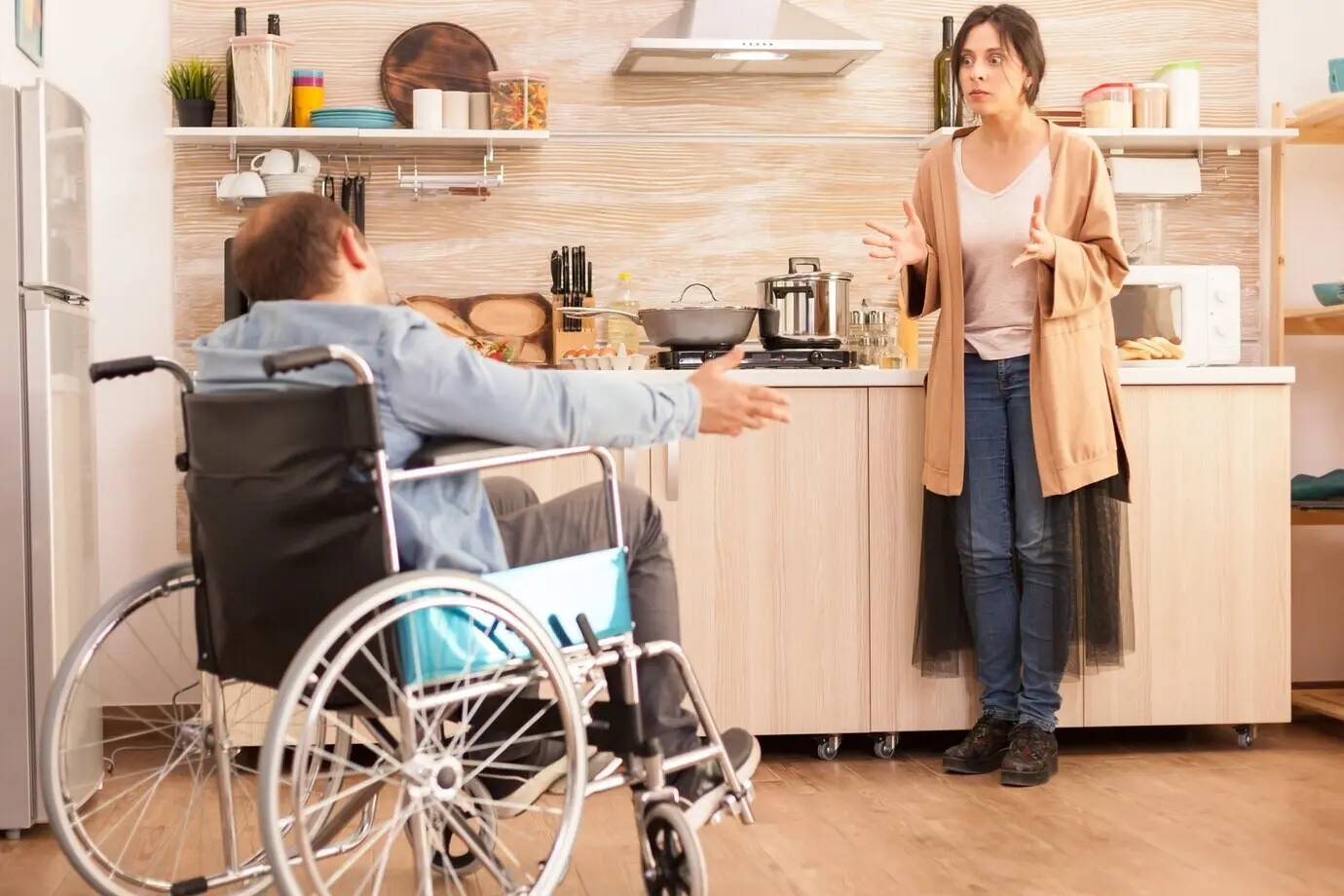 Wife looking angry at a disabled man in a wheelchair during an argument about their relationship in the kitchen. A disabled, paralyzed, handicapped man with a walking disability integrating after an accident.