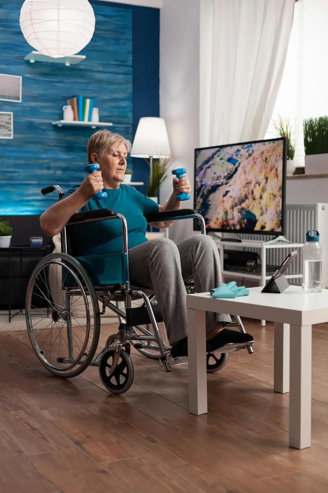 Disabled senior woman in a wheelchair stretching her arm muscles, performing resistance exercises.